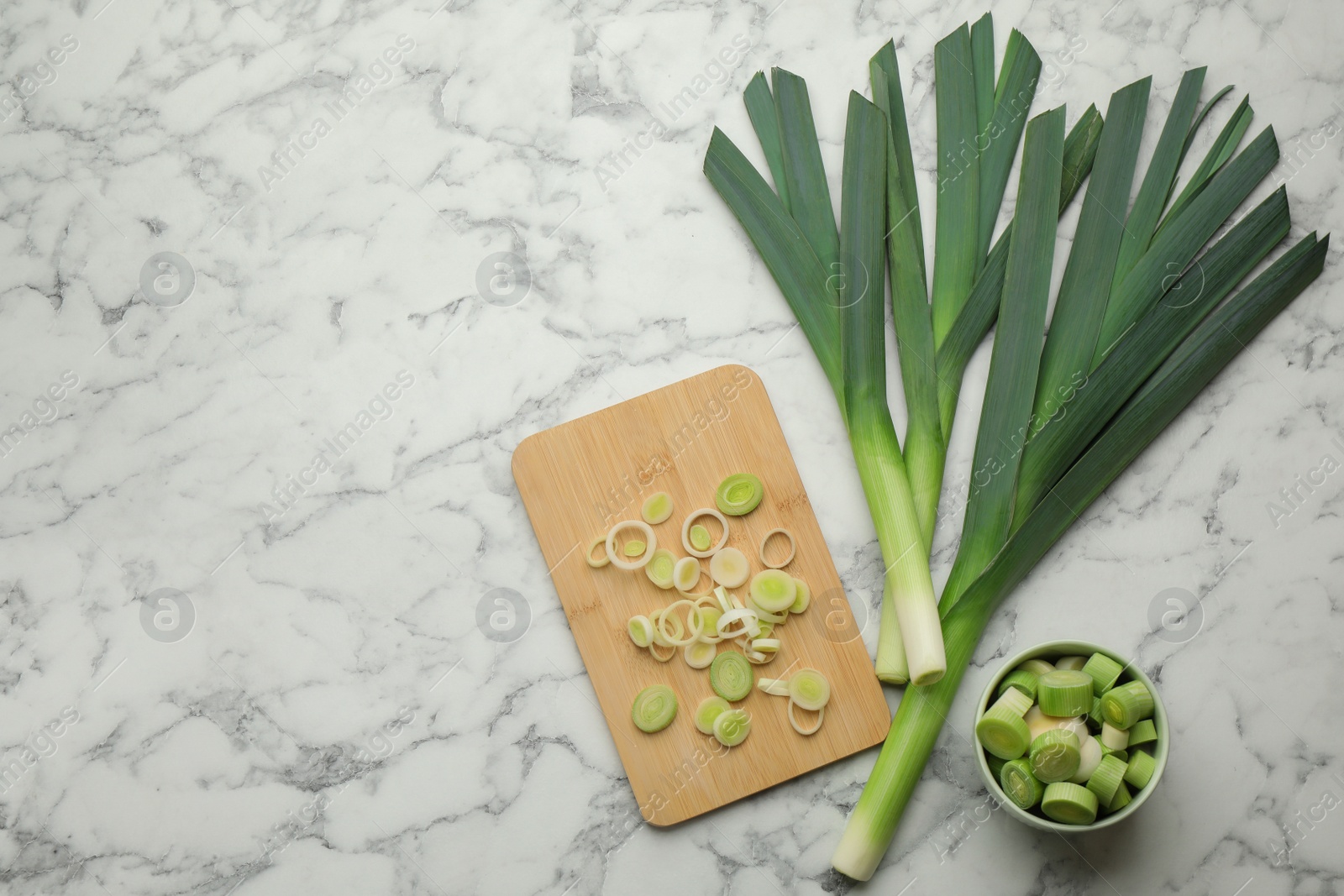 Photo of Whole and cut fresh leeks on white marble table, flat lay. Space for text
