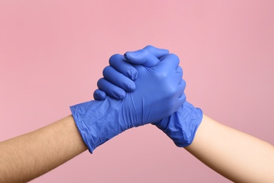 Photo of People in medical gloves shaking hands on pink background, closeup