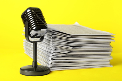 Photo of Newspapers and vintage microphone on yellow background. Journalist's work