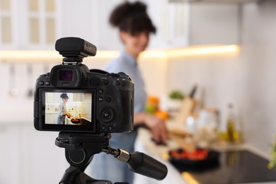 Photo of Food blogger cooking while recording video in kitchen, focus on camera