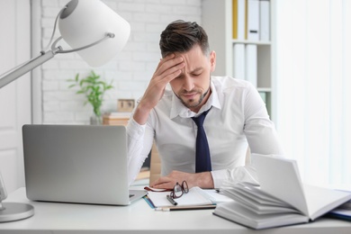 Photo of Man suffering from headache while sitting at table in office