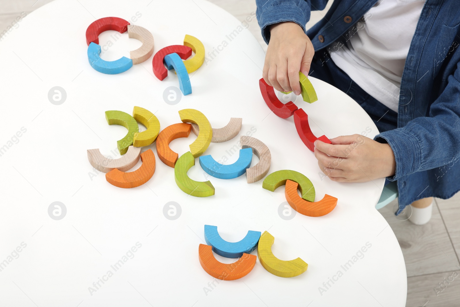 Photo of Motor skills development. Boy playing with colorful wooden arcs at white table, above view