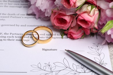 Photo of Marriage contract, golden wedding rings, pen and flowers, closeup