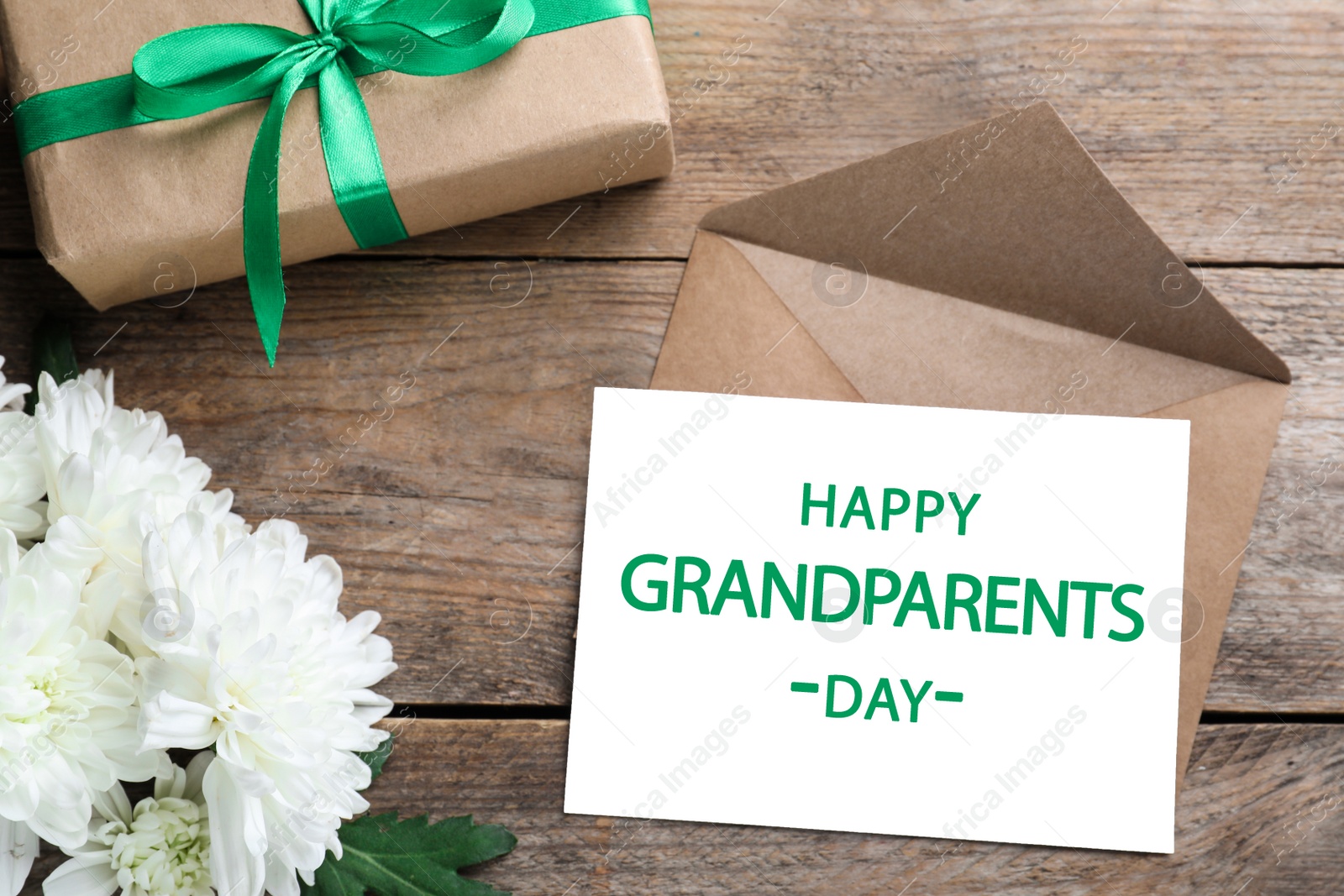 Photo of Beautiful white flowers, gift box and card with phrase Happy Grandparents Day on wooden table, flat lay