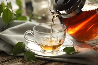 Photo of Pouring tea into cup on wooden table, closeup