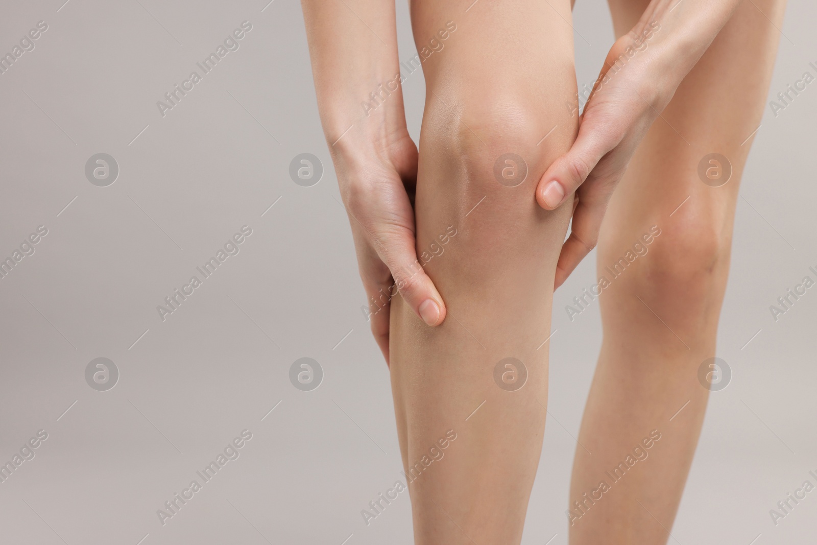 Photo of Woman suffering from leg pain on grey background, closeup. Space for text