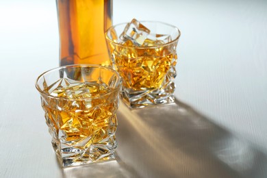Photo of Whiskey with ice cubes in glasses and bottle on white table. Space for text