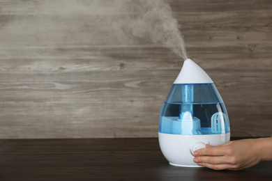 Photo of Woman using modern air humidifier at wooden table, closeup. Space for text
