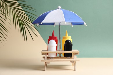 Photo of Wooden holder with different sauces, spices and toy umbrella on color background