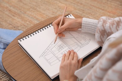 Image of Woman sketching building in notebook with pencil at home, closeup