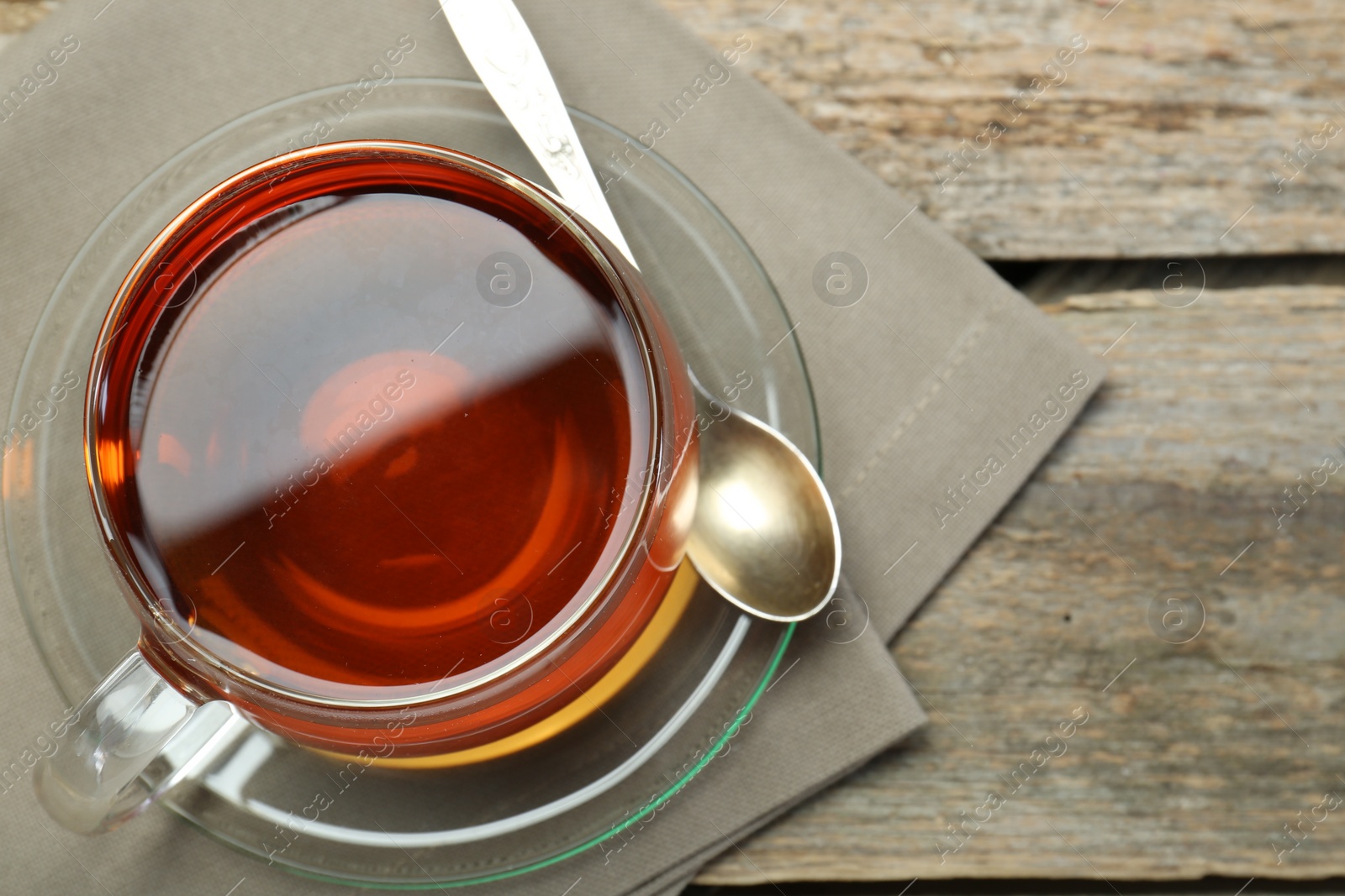 Photo of Aromatic tea in glass cup, spoon and napkin on wooden table, top view. Space for text