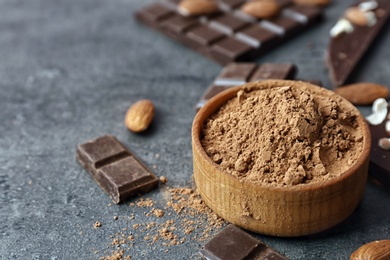 Photo of Bowl with cocoa powder and tasty chocolate on dark table, closeup