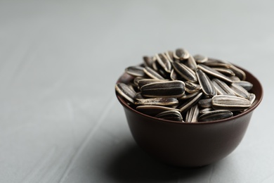 Photo of Raw sunflower seeds in bowl on grey table, closeup. Space for text