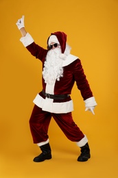 Photo of Santa Claus with headphones listening to Christmas music on yellow background