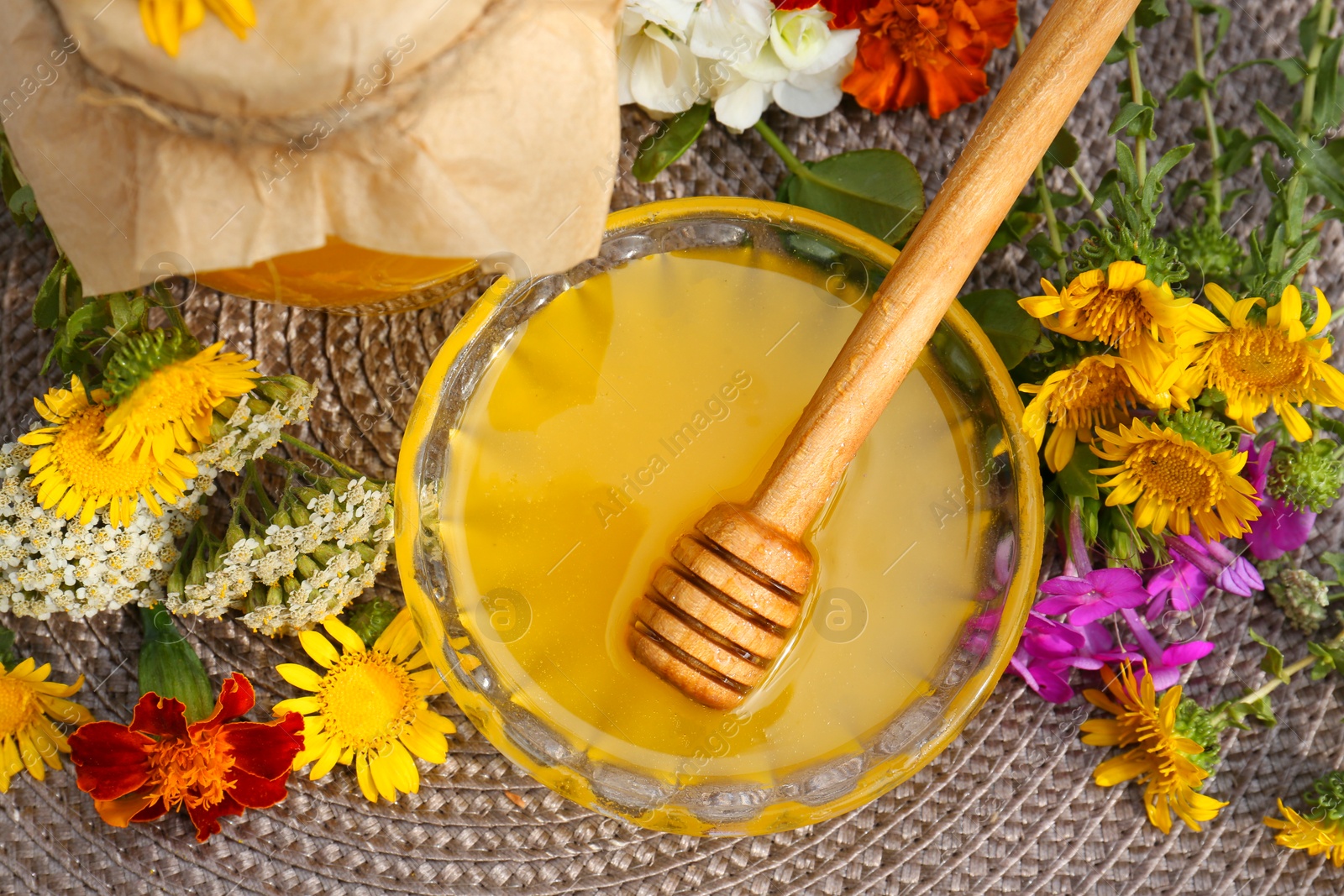 Photo of Delicious honey and dipper with different flowers on wicker mat, flat lay