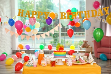 Bright birthday cake and other treats on table in decorated room