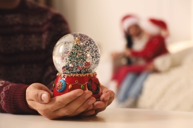 Man in warm Christmas sweater with snow globe at table, closeup
