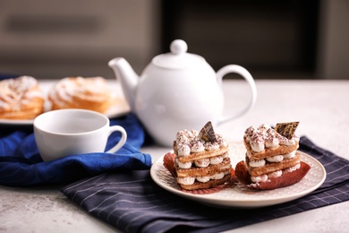 Photo of Plate with tasty pastries, teapot and cup on table