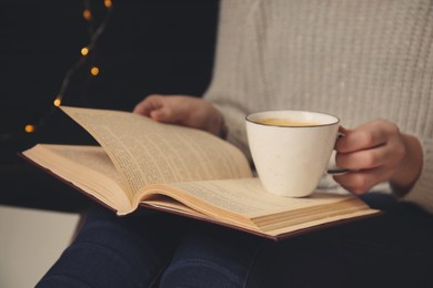 Image of Woman with cup of coffee reading book at home, closeup