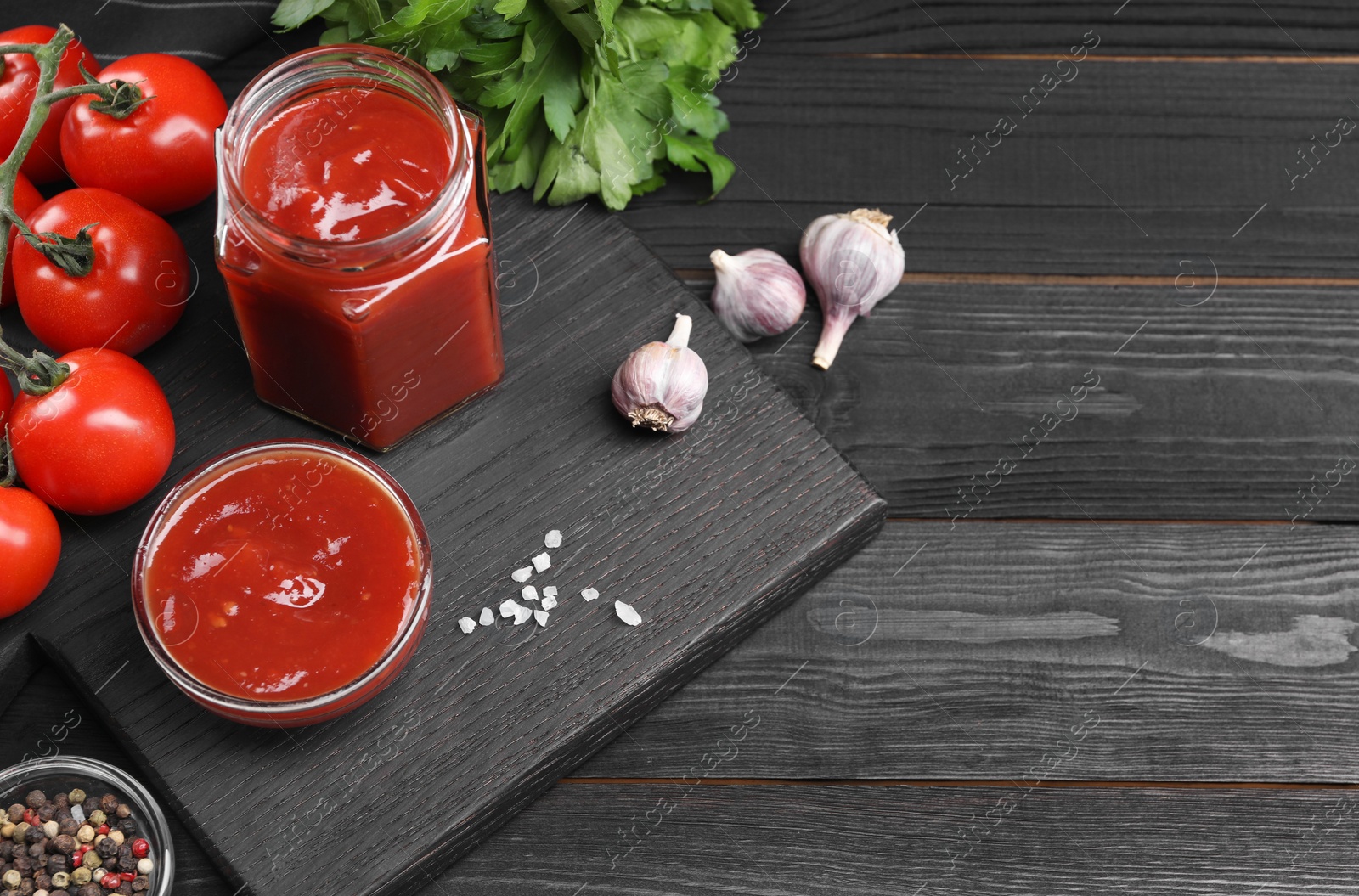 Photo of Flat lay composition with delicious ketchup, spices and products on black wooden table, space for text. Tomato sauce