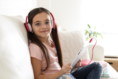 Cute little girl with headphones and tablet listening to audiobook at home