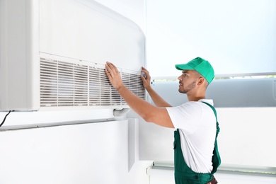 Photo of Professional technician maintaining modern air conditioner indoors