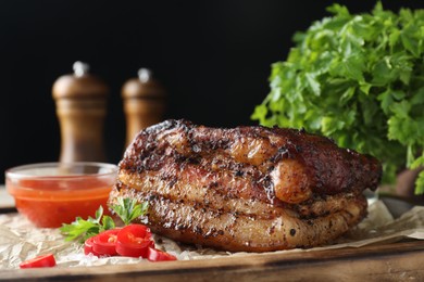 Photo of Piece of baked pork belly served with sauce and chili pepper on wooden board, closeup