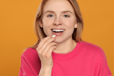 Happy young woman putting chewing gum into mouth on yellow background