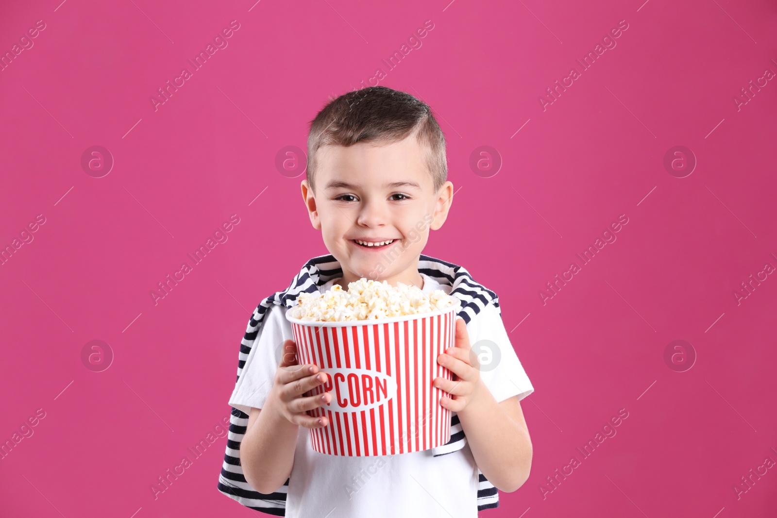Photo of Cute little boy with popcorn on color background