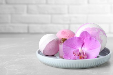 Photo of Bath bombs, bottle of oil and orchid flower on grey table, space for text