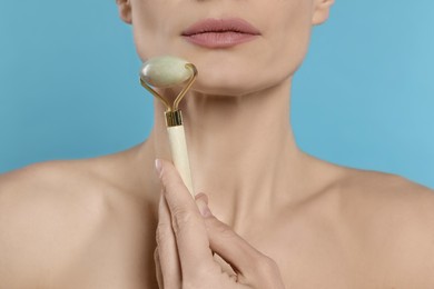 Woman massaging her face with jade roller on turquoise background, closeup