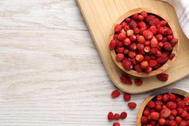 Photo of Fresh wild strawberries in bowls on white wooden table, flat lay. Space for text