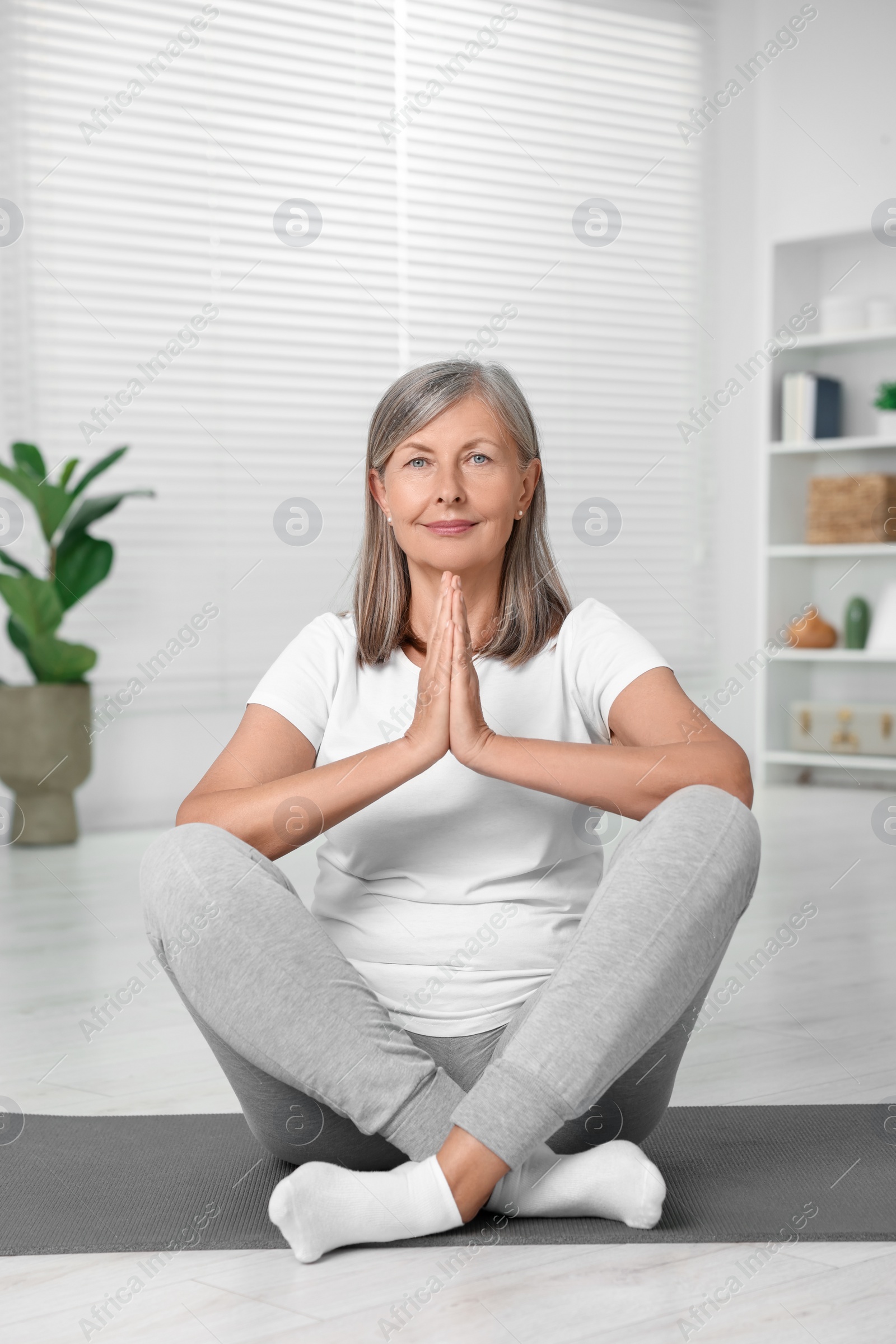 Photo of Happy senior woman practicing yoga on mat at home