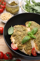 Delicious chicken breasts with pesto sauce, tomatoes and basil on table, closeup