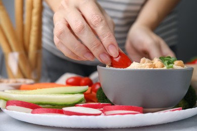 Woman dipping tomato into hummus at table, closeup