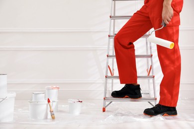 Worker with roller near ladder indoors, closeup. Space for text