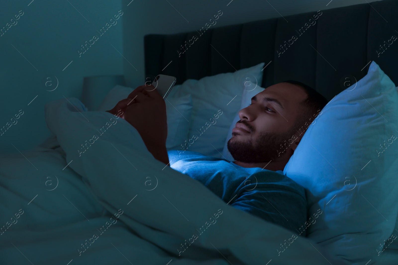 Photo of Young man using smartphone in bed at night. Internet addiction