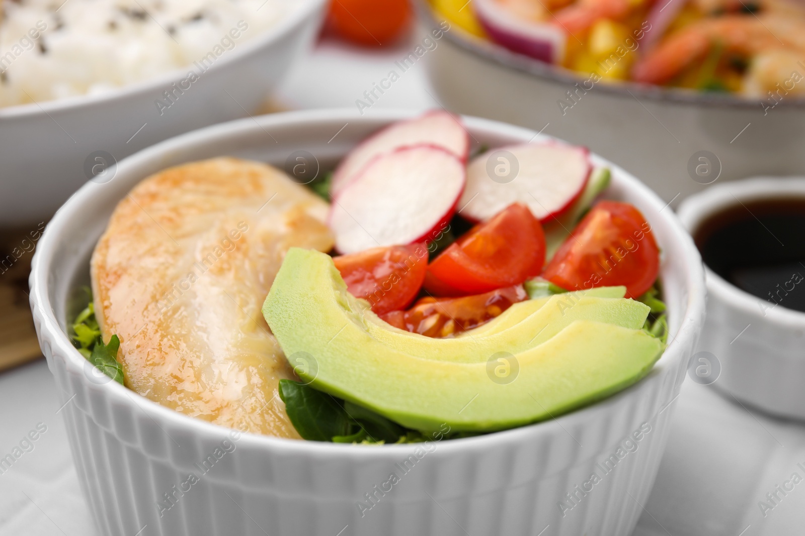 Photo of Delicious poke bowl with meat, avocado and vegetables on white table, closeup
