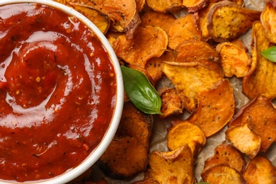 Photo of Top view of sweet potato chips and bowl with sauce on parchment, closeup