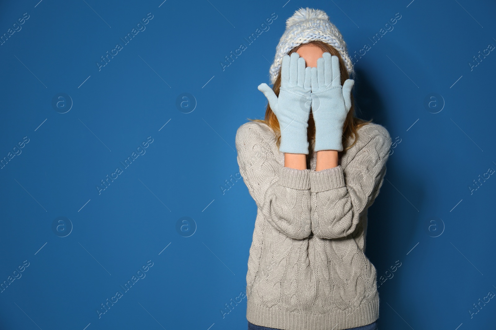 Image of Woman wearing warm sweater, knitted hat and mittens on blue background. Space for text