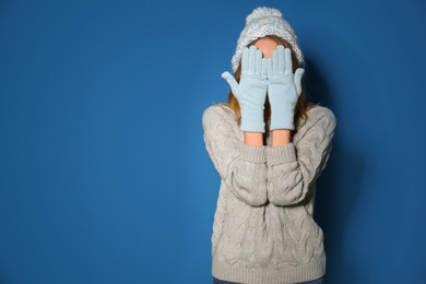 Image of Woman wearing warm sweater, knitted hat and mittens on blue background. Space for text