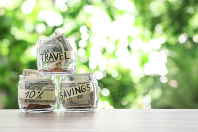 Photo of Glass jars with money for different needs on table against blurred background