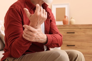 Senior man suffering from pain in his hand at home, closeup. Arthritis symptoms