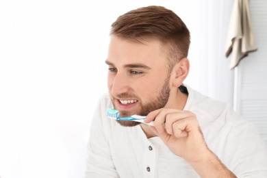 Photo of Young man cleaning teeth in light bathroom