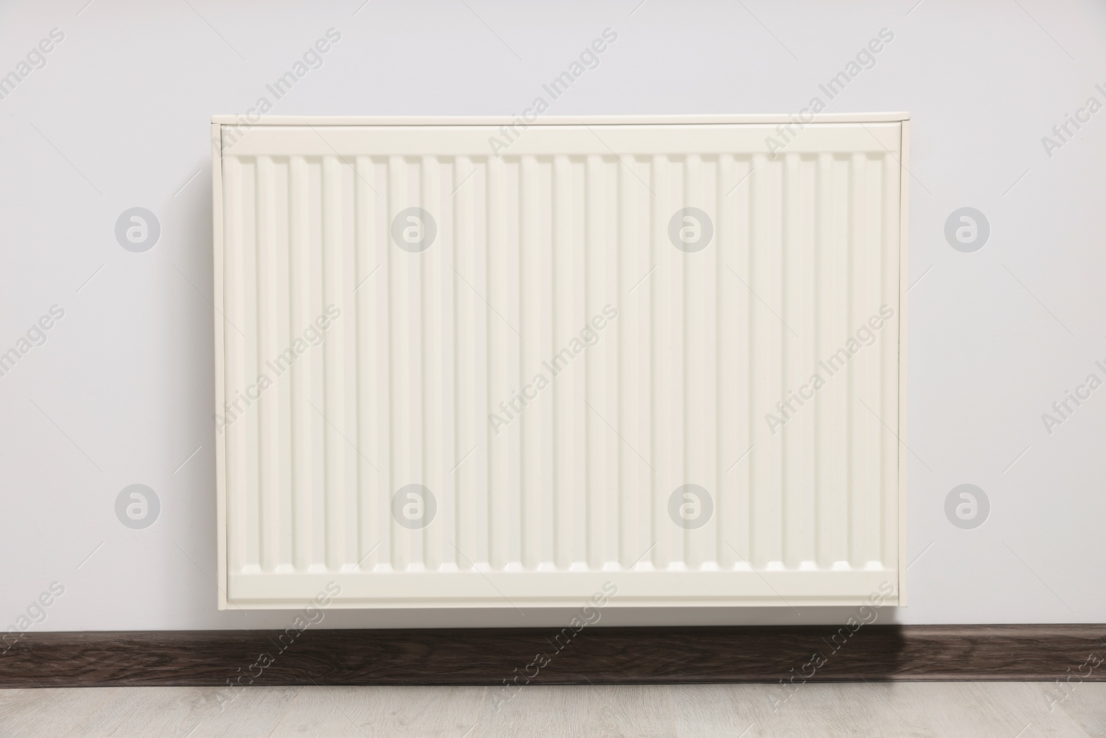 Photo of Modern radiator on white wall in room. Central heating system