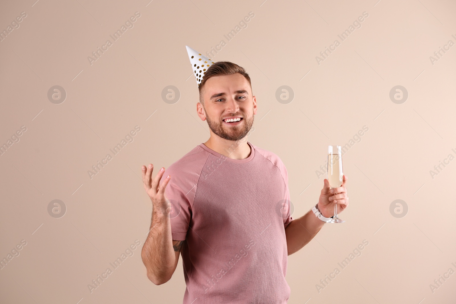 Photo of Portrait of happy man with party cap and champagne in glass on color background