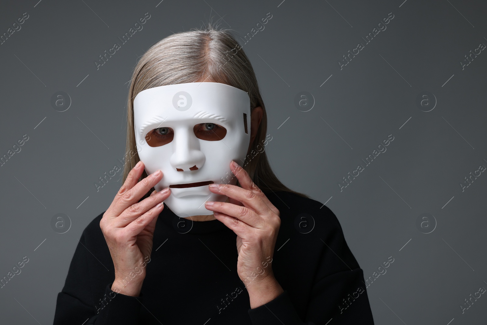 Photo of Multiple personality concept. Woman in mask on gray background, space for text