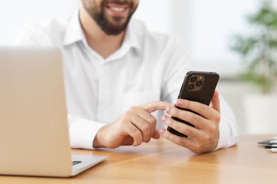 Young man using smartphone at wooden table in office, closeup