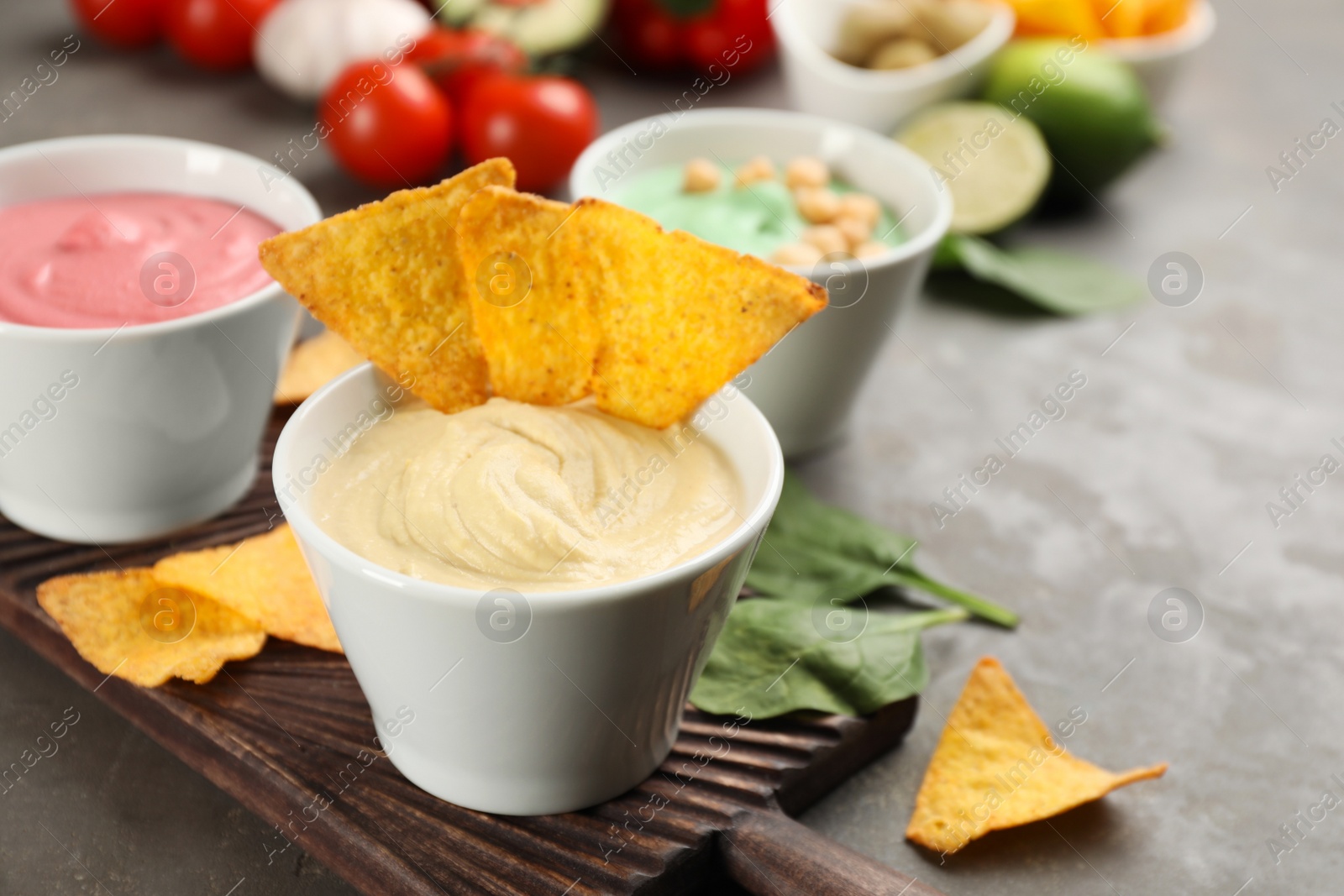 Photo of Different kinds of tasty hummus served with nachos on grey table, space for text