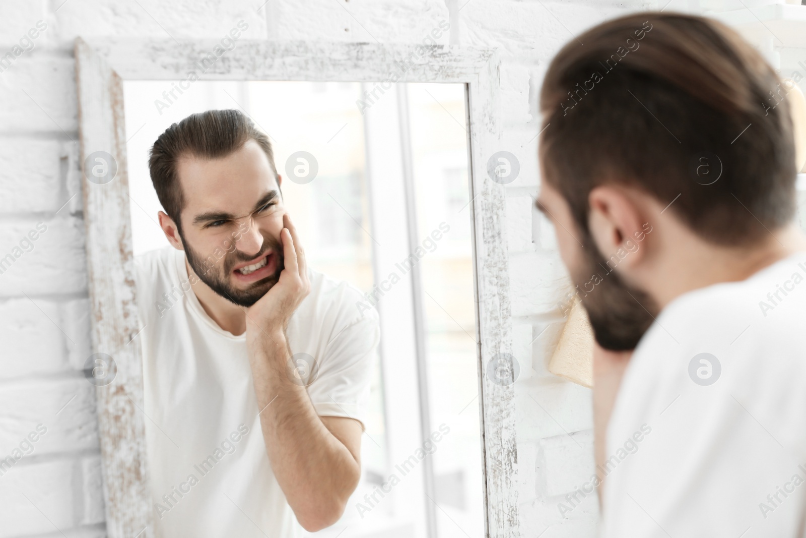 Photo of Young man suffering from toothache in bathroom